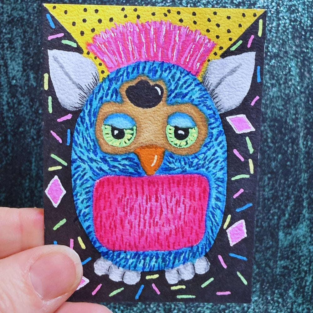 Colorful embroidered patch of an owl with a mohawk held by a hand on a textured fabric background.