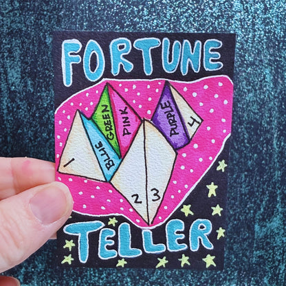 Colorful 'Fortune Teller' card with paper triangles and text on a textured blue background.