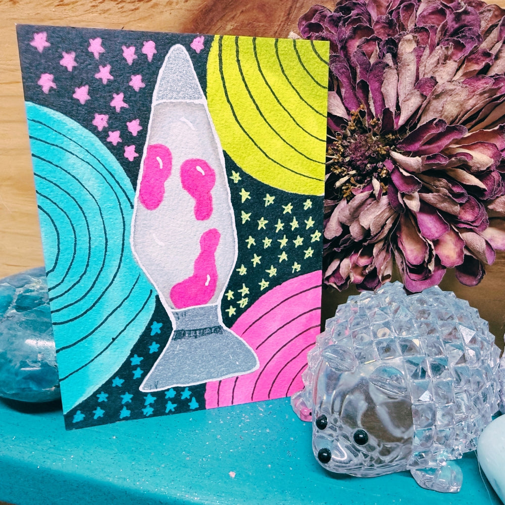 Colorful card with a lava lamp design, decorative flower, and crystal fish on a teal surface.