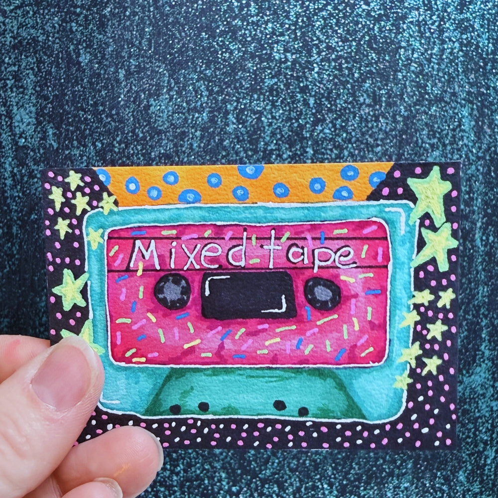 Colorful patch of a cassette tape labeled 'Mixed Tape' held against a textured blue background.