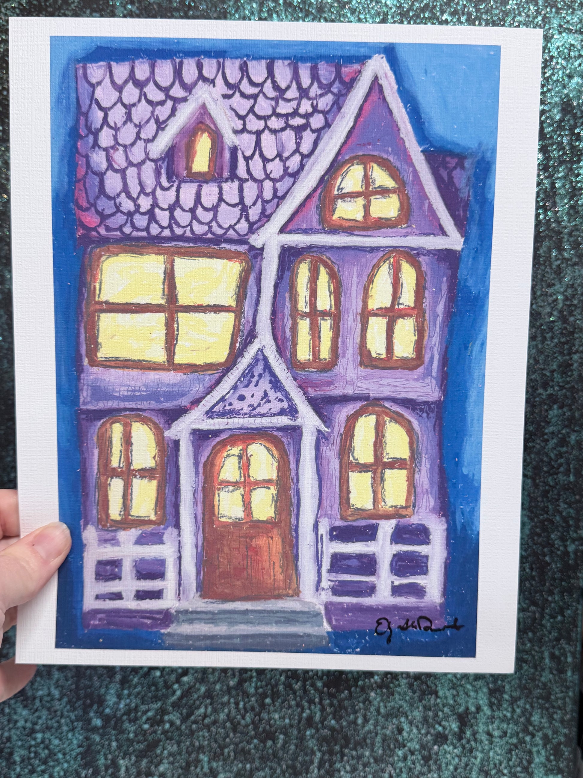Colorful house painting held by a hand on a textured green surface