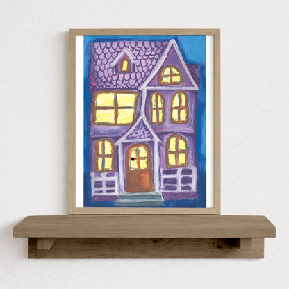 Framed artwork of a colorful house on a wooden shelf against a white wall