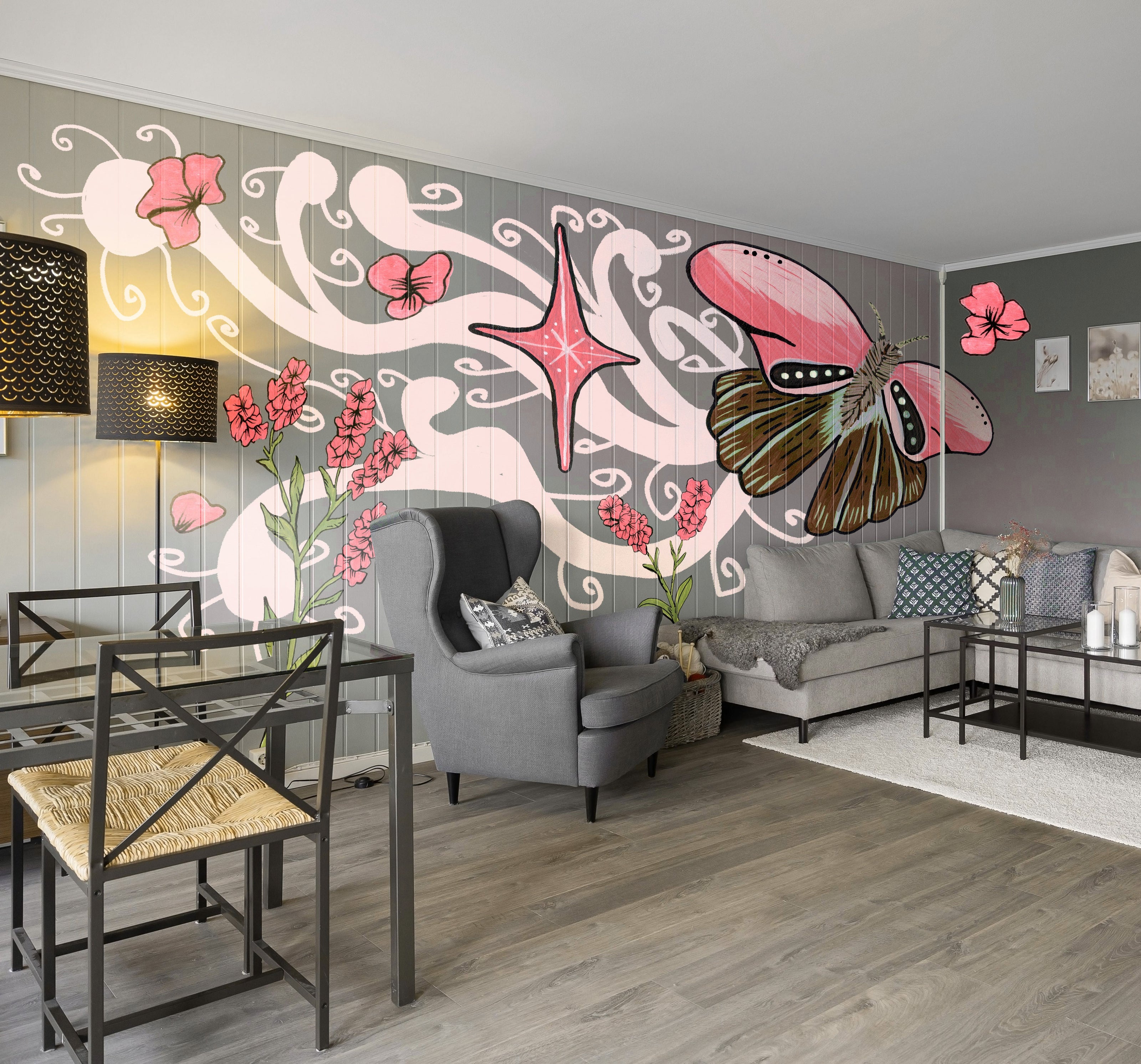 A modern living room featuring a large decorative wall mural with a pink butterfly, pink flowers, and swirling white patterns on a gray background. The room includes a gray sofa with patterned pillows, a gray armchair, black-framed glass tables, a white rug, and gray wood-look flooring.